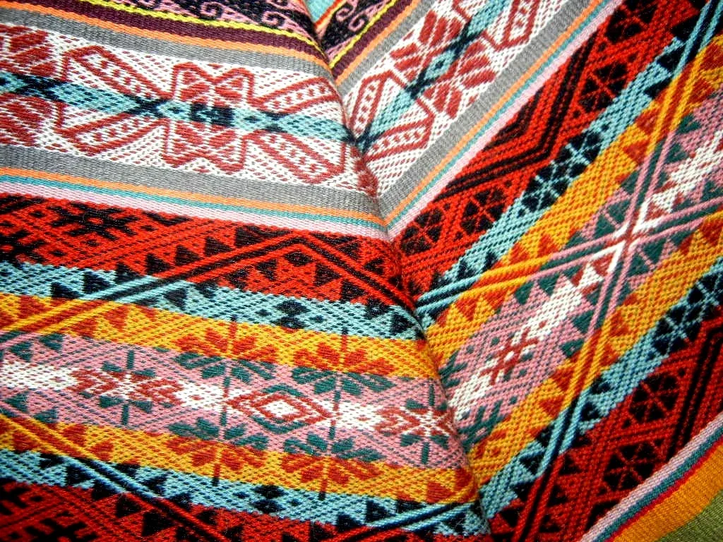 Turuncu, kırmızı, turkuaz, sarı ve pembe şeritlerden oluşan, geometrik desenli dokuma kumaşın yakın planı.